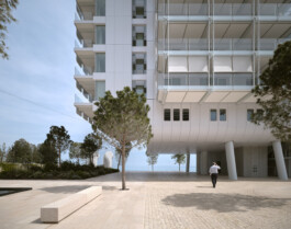 Mareterra, Renzo Piano Building Workshop, Monaco, 2024 — walking beneath elevated building volume on pilotis with sea view 